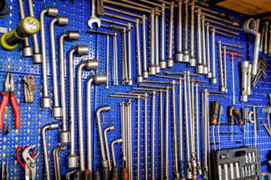 Makine atölyesinden bir takım anahtar ve aletler. Meşale, İngiliz anahtarı ve kerpetenle mavi arka planda asılı duruyor. Çalışmak, sanat ve el sanatları için mükemmel bir çekim..