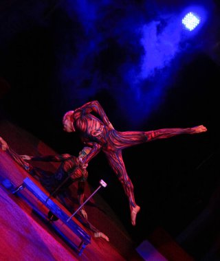 Neon kostümlü ikiz akrobatlar kollarında, ultraviyole makyajlı