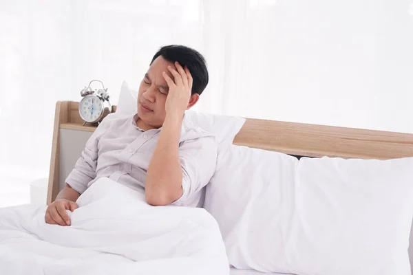 Asian man wake up in the morning. He discomfort and headache on bed in bedroom. Healthcare concept.