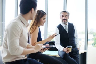 Gülümseyen Asyalı takım ve Kafkasyalı kıdemli patron, iş adamı takım çalışması, dinlendirici ve beyin fırtınası. İş kadını elinde akıllı telefon tutuyor ve ofisteki haberlerden bahsediyor. Kafkasyalı adama odaklan..