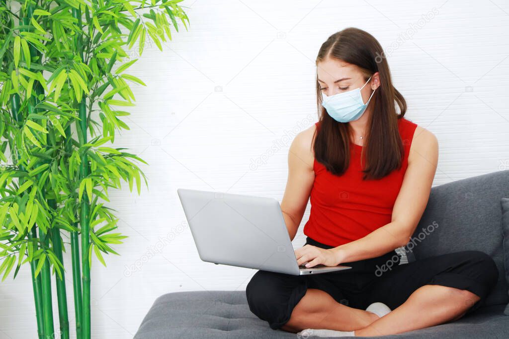 Young Caucasian woman wearing mask prevent covid 19 Virus and working with laptop in living room at home or workpalce at office. Work from home and quarantine concept.