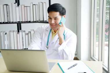 Gülümseyen Asyalı profesyonel psikiyatrist ya da nörolog, akıl sağlığı sorunları olan hastaları tedavi etmek için akıllı telefondan arıyor ve tavsiyelerde bulunuyor. Sağlık ve teknoloji kavramı.