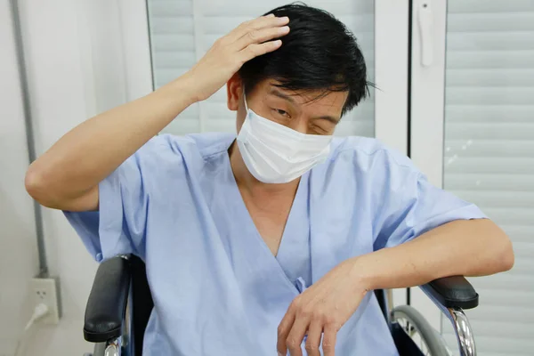 Asian Old man Wearing a mask to prevent disease and Covid 19 is sitting on wheelchair. He is Sick and headache for seriously ill in Hospital. Healthcare and Elderly society Concept