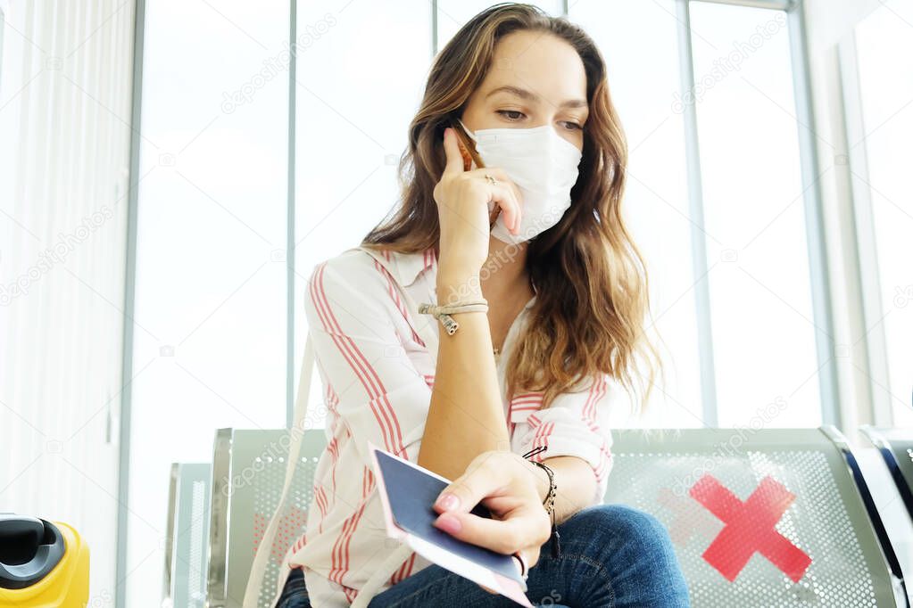 Caucasian traveler woman is wearing mask for prevent covid-19 and calling with smartphone. She is sitting on passenger in airport. Healthcare and jouney business trip on vacation concept.