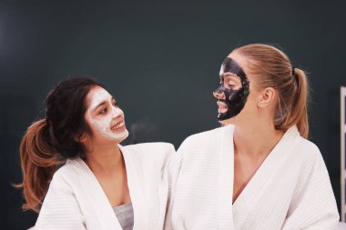 Beyaz bornoz ve başörtüsü içinde gülümseyen Kafkasyalı ve Asyalı kadın spa 'da yatakta dinleniyor ve sarılıyor. Lezbiyen yaşam tarzı ve güzellik salonu.