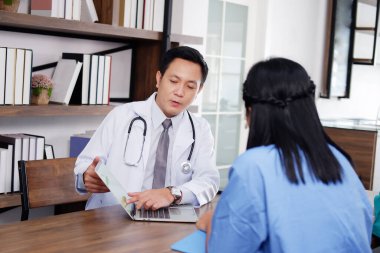 Asyalı başhekim, cerrah kadınla görüşüyor. Doktor kadın mavi ameliyat elbisesi giyiyor. Tıbbi ekip hastanedeki hastaları tedavi etmek için dizüstü bilgisayarla konuşuyor ve araştırıyor..