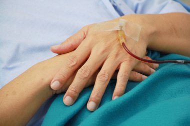 Asyalı ihtiyarın eli kapalıyken haspital yatağında salin veriyor. Yaşlılık konseptinde yaşlıların rahatsızlığı.