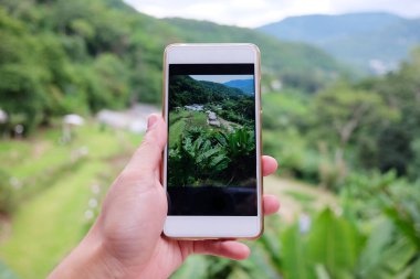 Akıllı telefonlu bir kadın fotoğraf çekmek için güzel bir manzara vadisi dağı yeşil tepe ve yağmur mevsiminde orman tepesinde Hill kabilesi köyü ile Tayland 'da..
