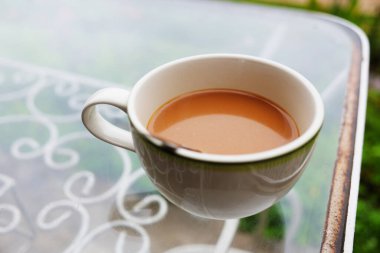 Tropikal bahçede cam masada seramik bir fincan sıcak kahve.