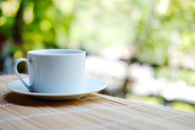 Beyaz seramik fincan sıcak kahveyi el ele tutuşarak dokuma hasırının üzerinde ve bahçede doğal ışık sabahıyla. Kafein içecekleri taze bir hisse neden olur..