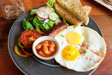 Lezzetli kızarmış yumurta, füme sosisli tereyağlı ekmek soslu ve siyah tabakta sebzeli ev yapımı kahvaltı..