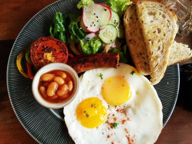 Lezzetli kızarmış yumurta, füme sosisli tereyağlı ekmek soslu ve siyah tabakta sebzeli ev yapımı kahvaltı..