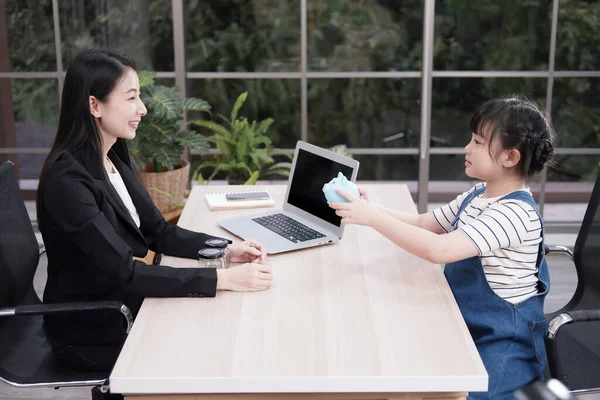 Asian little asian girl child is holding blue piggy bank and bring money deposit with woman Bank clerk is smiling in office. Child is learning business for saving money in the future concept.