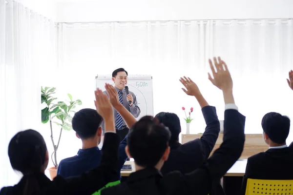 Senior Asian Lecturer is lecturing about business and stock market topics and business people are having a seminar and raising hands agree with teacher in the economics class in meeting room.