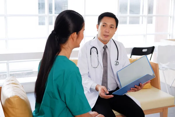 Asian chief physician man is brainstorming with surgeon doctor woman wears green surgical gown. Medical team are talking and researching with laptop for treatment in meeting room at hospital.