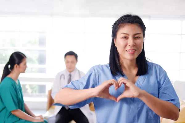 アジアの外科医の女性は青と緑の外科用ガウンを着ている 彼女は笑顔と手作りの心と患者の世話をしています アジアの主任医師 Manmedicalチームが病院の会議室で — ストック写真
