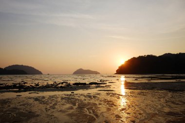 Tayland 'daki deniz suyuna yansıyan parlak altın renkleriyle sakin bir plajın üzerinde çarpıcı bir günbatımı ile plajda güzel bir alacakaranlık.