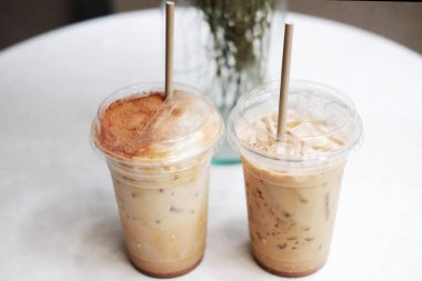İki plastik bardak buzlu latte kahve ve açık hava bahçesi için beyaz masa üzerine süslenmiş vazoda kuru çimen çiçeği.