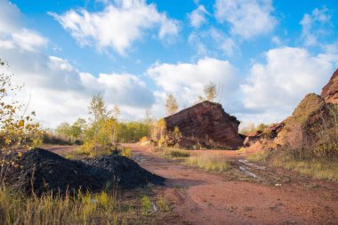 Sonbahar ağaçları ve mavi bulutlu gökyüzü olan kırmızı dağlar. Madenlerden kömür çıkardıktan sonra renkli atık yığınları.
