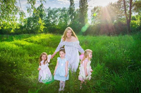 A kind sorceress and little girls elves with wings on a green lawn in the sunlight. Selective focus. Blurred background.