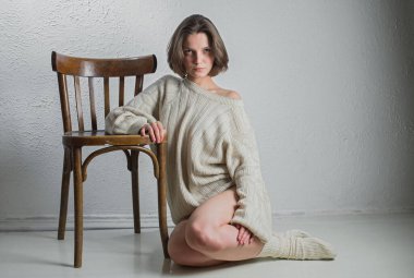 Sıcak örgü kazaklı genç ve güzel bir kız ahşap bir sandalyenin yanında oturuyor. Hafif arkaplan.