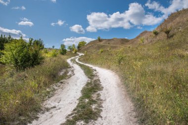 Tepelerin arasında bir patika. Yaz mavi bulutlu gökyüzü.