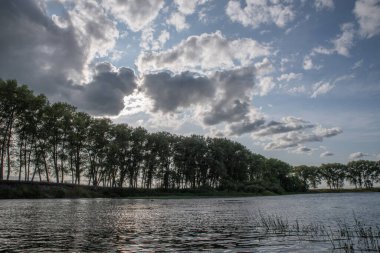 Akşamları bulutlu gökyüzüne karşı nehrin üzerinde bir sıra ağaç..