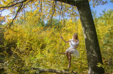 Kız sonbahar ormanında bir salıncakta sallanıyor sarı-altın yaprakların arka planında. Seçici odak.