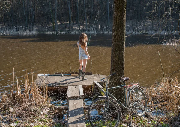 夕暮れ時の暖かい夏の日に湖のそばでデニムのショートパンツと古い自転車の女の子 — ストック写真