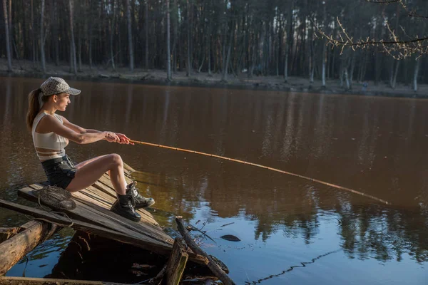 一个在木码头上拿着钓竿的女孩正在一个森林湖里钓鱼 — 图库照片