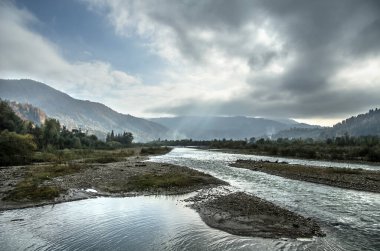 Dağların arasında renkli sonbahar yaprakları ve parlak gökyüzü olan bir nehir..