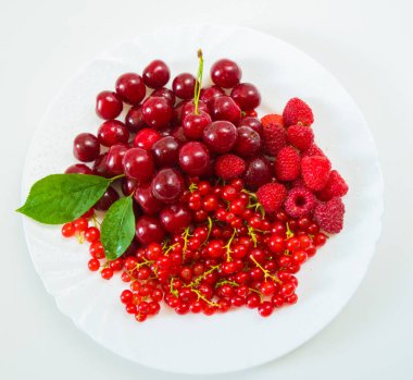 Beyaz arka planda tabakta çeşitli kırmızı taze meyveler..