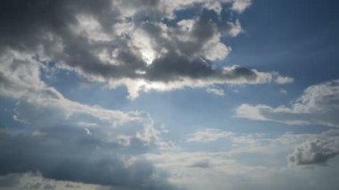 Dark cumulus clouds arise and move in the blue sky under the sun. The sun's rays shine through the clouds and change shape. Majestic amazing sky. Cloud space