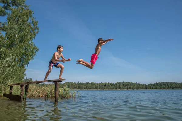 Boys jump into the water from a wooden bridge.