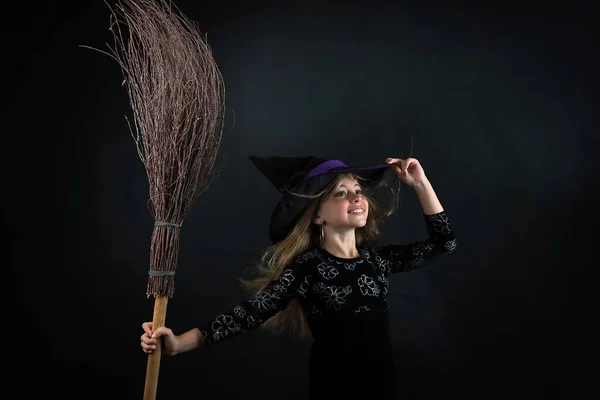 Egy Kislány Sötét Háttérben Boszorkányjelmezben Széles Karimájú Kalapban Seprűvel Halloweenkor — Stock Fotó