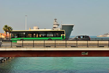 Bir sahil kasabasında bir köprü üzerinde dolaşan araçlar da bir donanma gemisi görebilirsiniz