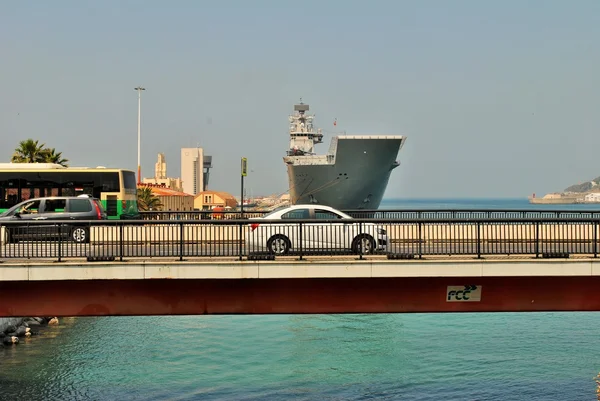 Los vehículos que circulan en un puente en una ciudad costera también pueden ver un barco de la marina —  Fotos de Stock