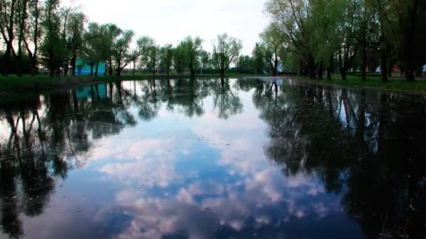 Белые облака, плавающие в пруду парка отражение на фоне шоссе, по которому автомобили идут — стоковое видео