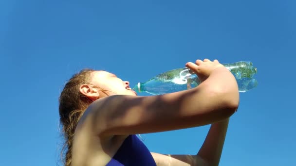 Jong meisje dat mineraalwater drinkt op het strand. slow motion — Stockvideo