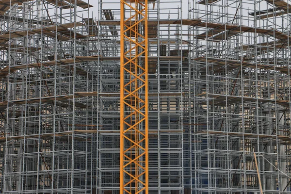 Construction crane in front of a building with scaffolding covered with tarpaulin