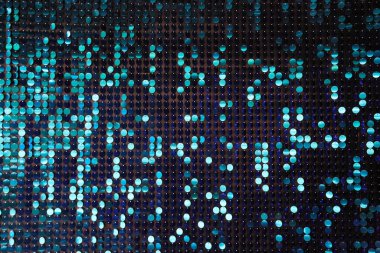 Arka planın parlak dokusu, balık pulu gibi kumaşa dikilmiş yuvarlak mavi pullar.