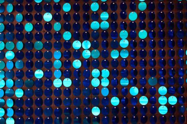 Arka planın parlak dokusu, balık pulu gibi kumaşa dikilmiş yuvarlak mavi pullar.