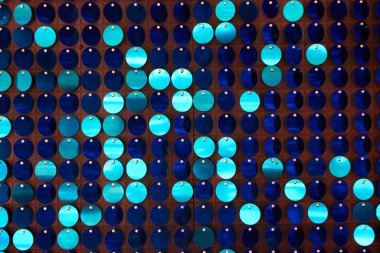 Arka planın parlak dokusu, balık pulu gibi kumaşa dikilmiş yuvarlak mavi pullar.