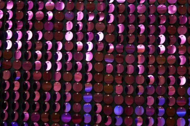 Arka planın parlak dokusu, balık pulu gibi kumaşa dikilmiş yuvarlak mor pullar.