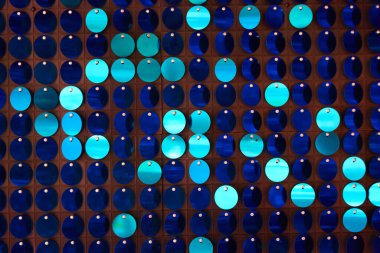 Arka planın parlak dokusu, balık pulu gibi kumaşa dikilmiş yuvarlak mavi pullar.