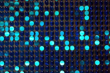 Arka planın parlak dokusu, balık pulu gibi kumaşa dikilmiş yuvarlak mavi pullar.