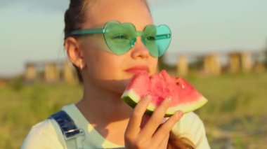 Bir kız gün batımında parkta lezzetli bir karpuz yiyor.