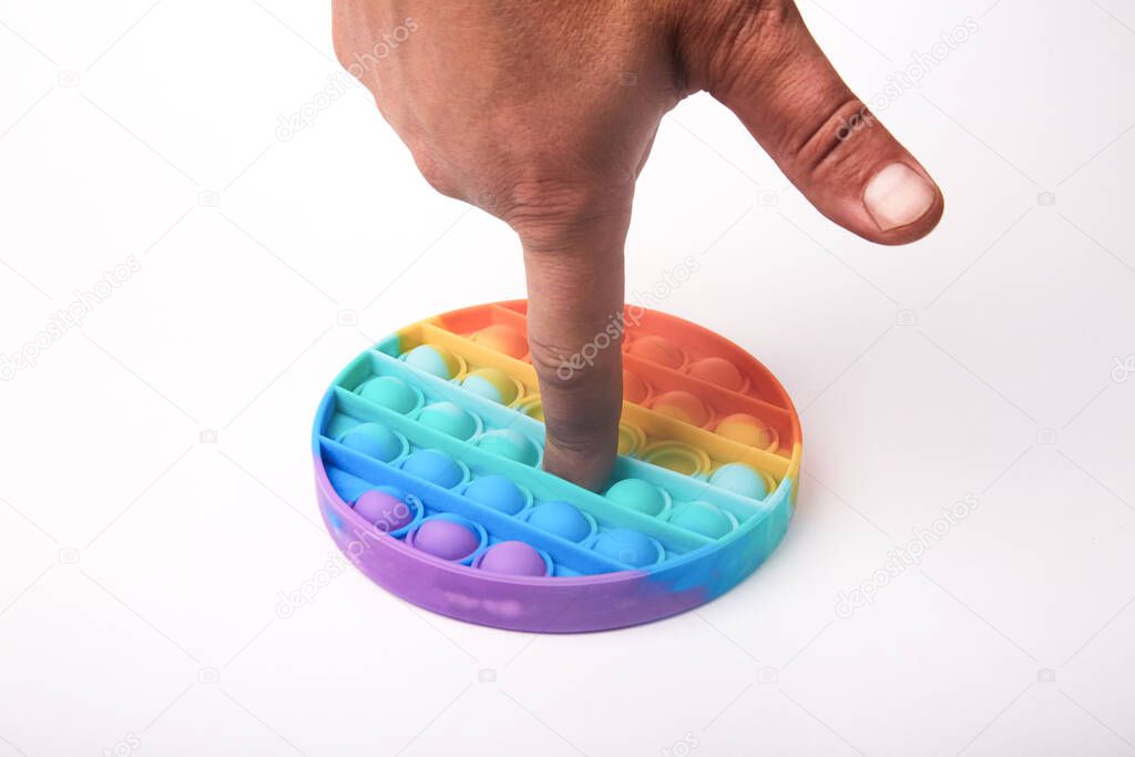 A finger presses on a multi-colored Pop it toy on a white background
