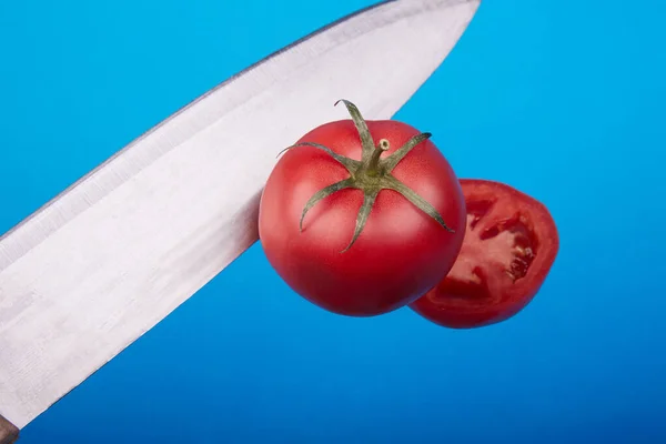 Olgun bir domates mavi arka planda havayı kesiyor. — Stok fotoğraf