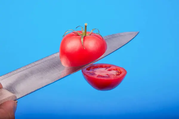 Olgun bir domates mavi arka planda havayı kesiyor. — Stok fotoğraf